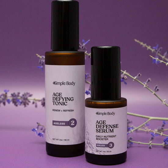 Simple Body Ageless duo products including Age Defying Tonic and Age Defense Serum both with purple labels photographed on a rich purple background with a stem of lavender buds behind them.