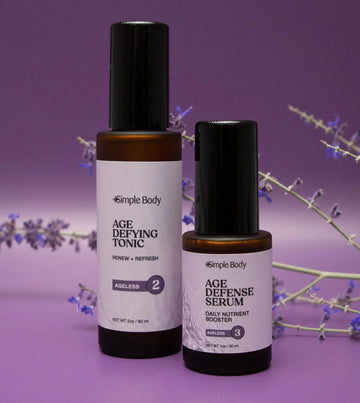 Simple Body Ageless duo products including Age Defying Tonic and Age Defense Serum both with purple labels photographed on a rich purple background with a stem of lavender buds behind them.
