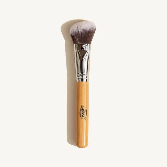 A photo of Pure Anada's vegan Angled Makeup Brush which is brown that fades to white on the ends with a wooden handle on a tan background.