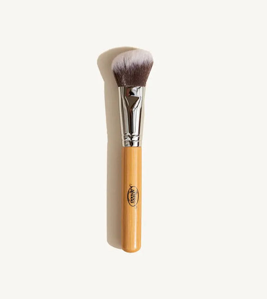 A photo of Pure Anada's vegan Angled Makeup Brush which is brown that fades to white on the ends with a wooden handle on a tan background.