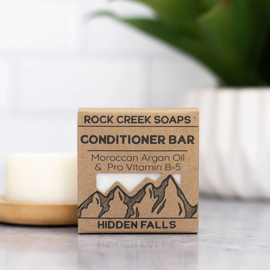 Rock Creek Soaps conditioner bar packaging with a candle and plant in the background