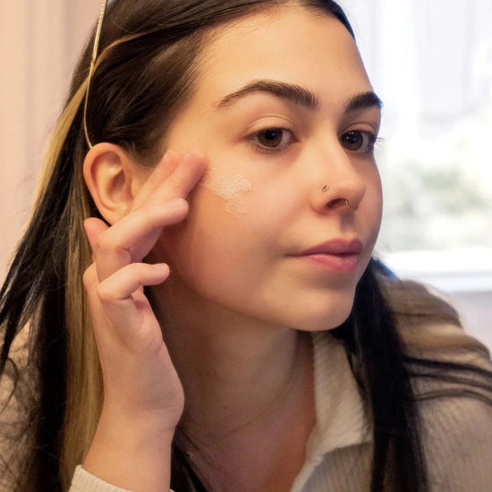 A woman demonstrating the texture of the Simple Body Bamboo Face Polish with long dark hair and dark eyes.