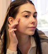 A woman demonstrating the texture of the Simple Body Bamboo Face Polish with long dark hair and dark eyes.