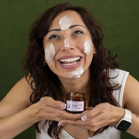 Saba holding a jar of Simple Body Bamboo Face Polish while applying and looking up and smiling.