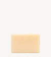 A handmade bar of soap with a yellow color and an embossed design on it, placed against a tan background.