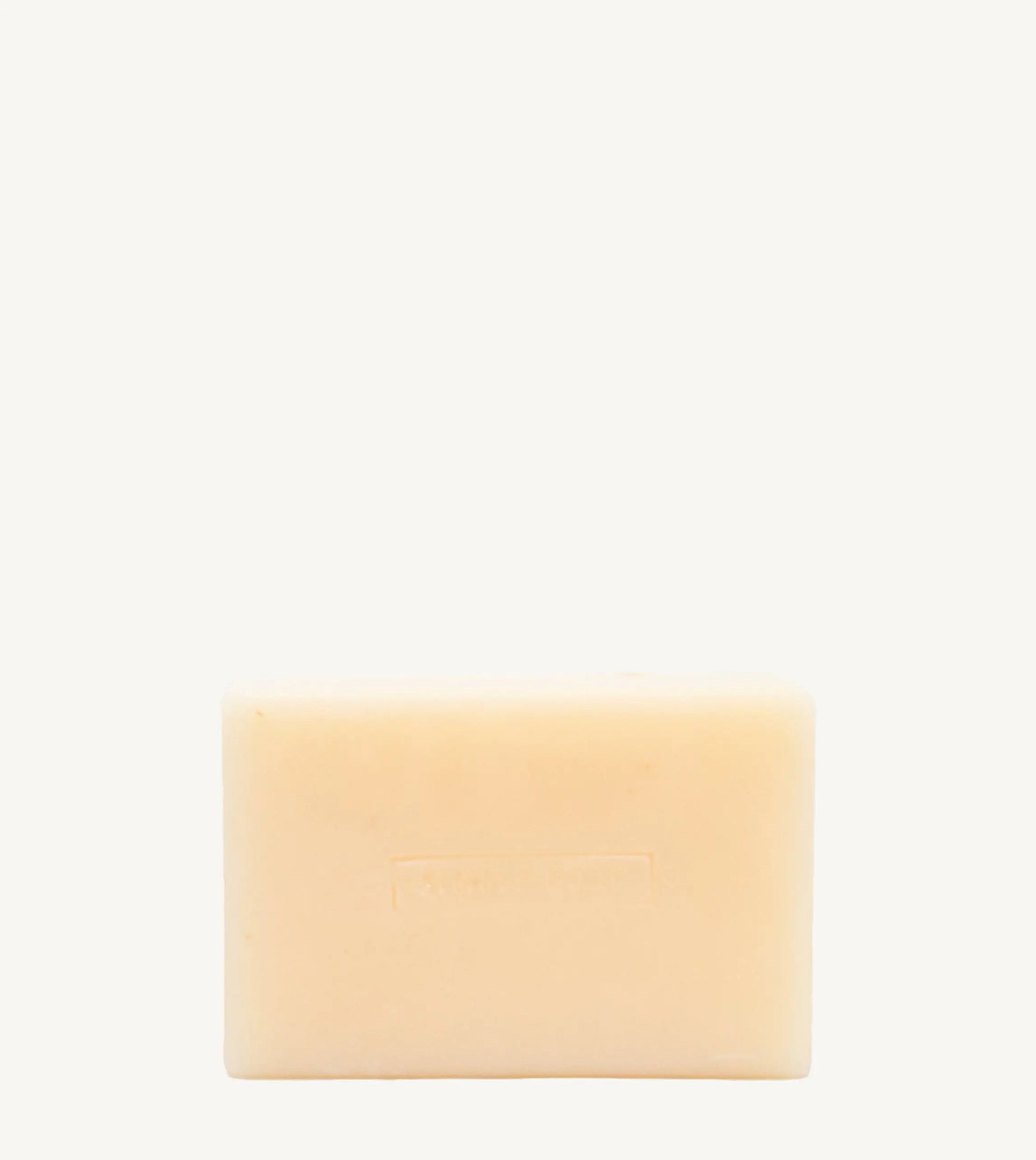 A handmade bar of soap with a yellow color and an embossed design on it, placed against a tan background.