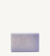 A handmade bar of soap with a purple color and an embossed design on it, placed against a tan background.