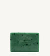 A handmade bar of soap with a green color and an embossed design on it, placed against a tan background.