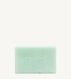 A handmade bar of soap with a mint color and an embossed design on it, placed against a tan background.