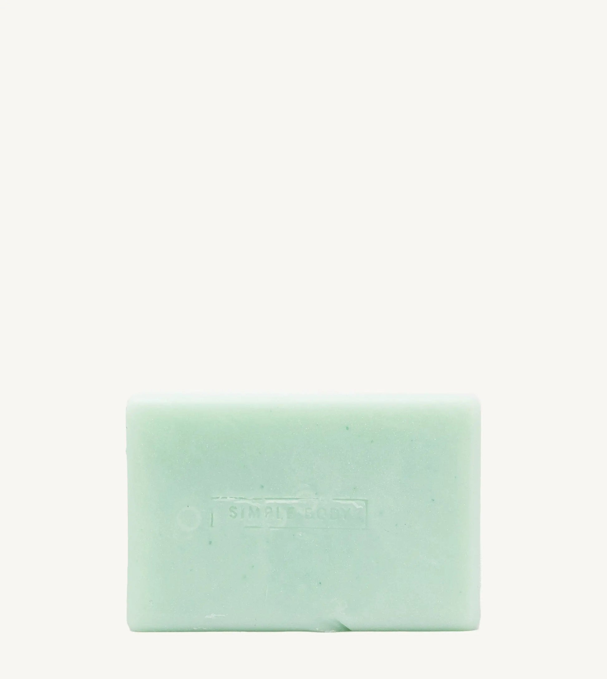A handmade bar of soap with a mint color and an embossed design on it, placed against a tan background.