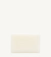 A handmade bar of soap with an off-white color and an embossed design on it, placed against a tan background.