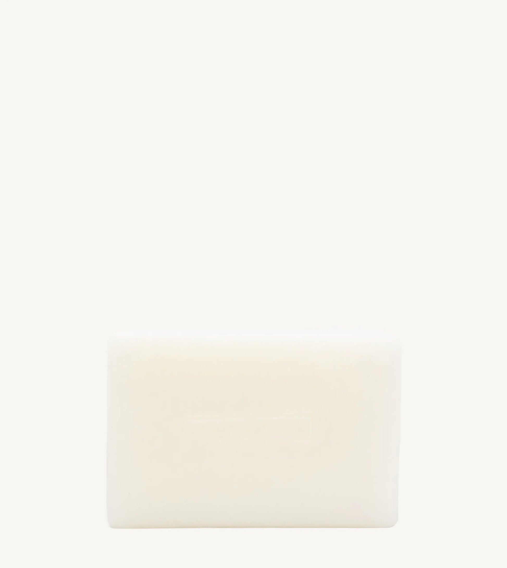 A handmade bar of soap with an off-white color and an embossed design on it, placed against a tan background.