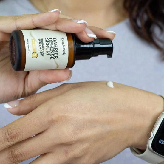 Hand applying Simple Body Barrier Defense Serum to another hand with a blurred background