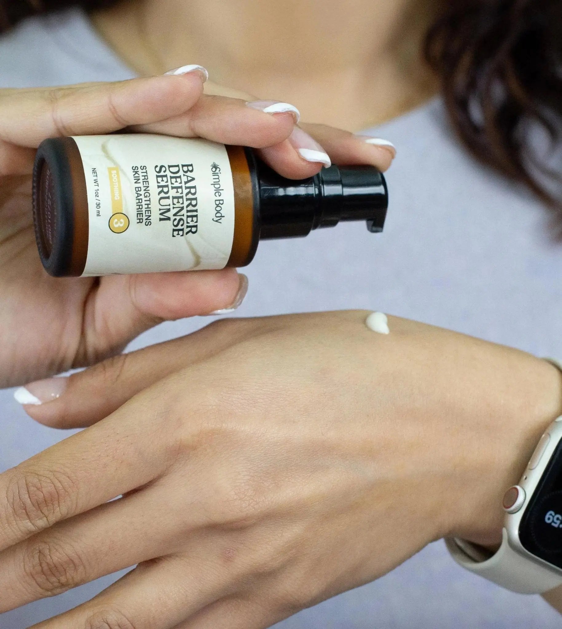 Hand applying Simple Body Barrier Defense Serum to another hand with a blurred background