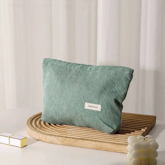 Green corduroy cosmetic bag on a wooden tray with a white curtain background