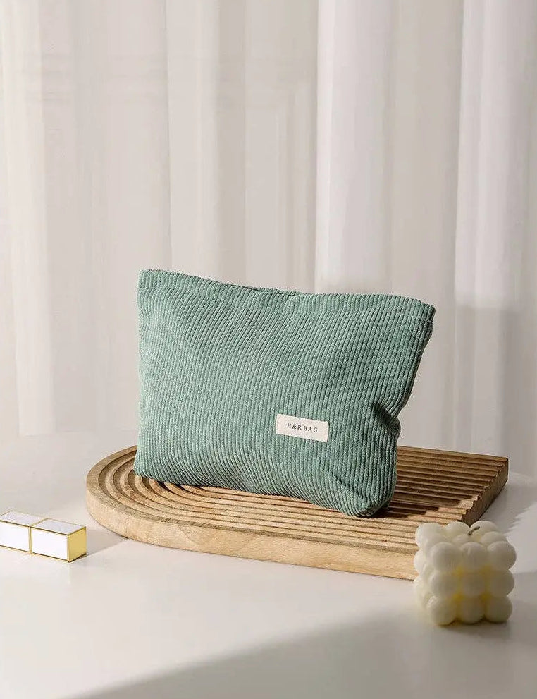 Green corduroy cosmetic bag on a wooden tray with a white curtain background