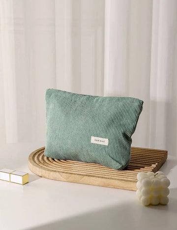 Green corduroy cosmetic bag on a wooden tray with a white curtain background