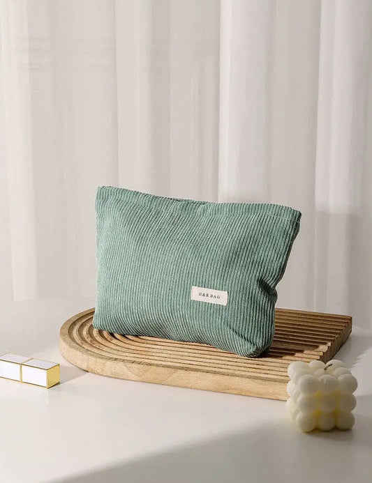 Green corduroy cosmetic bag on a wooden tray with a white curtain background