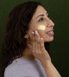 A woman looking sideways applying Simple Body Beauty Balm to her cheek which is a yellow, creamy texture.