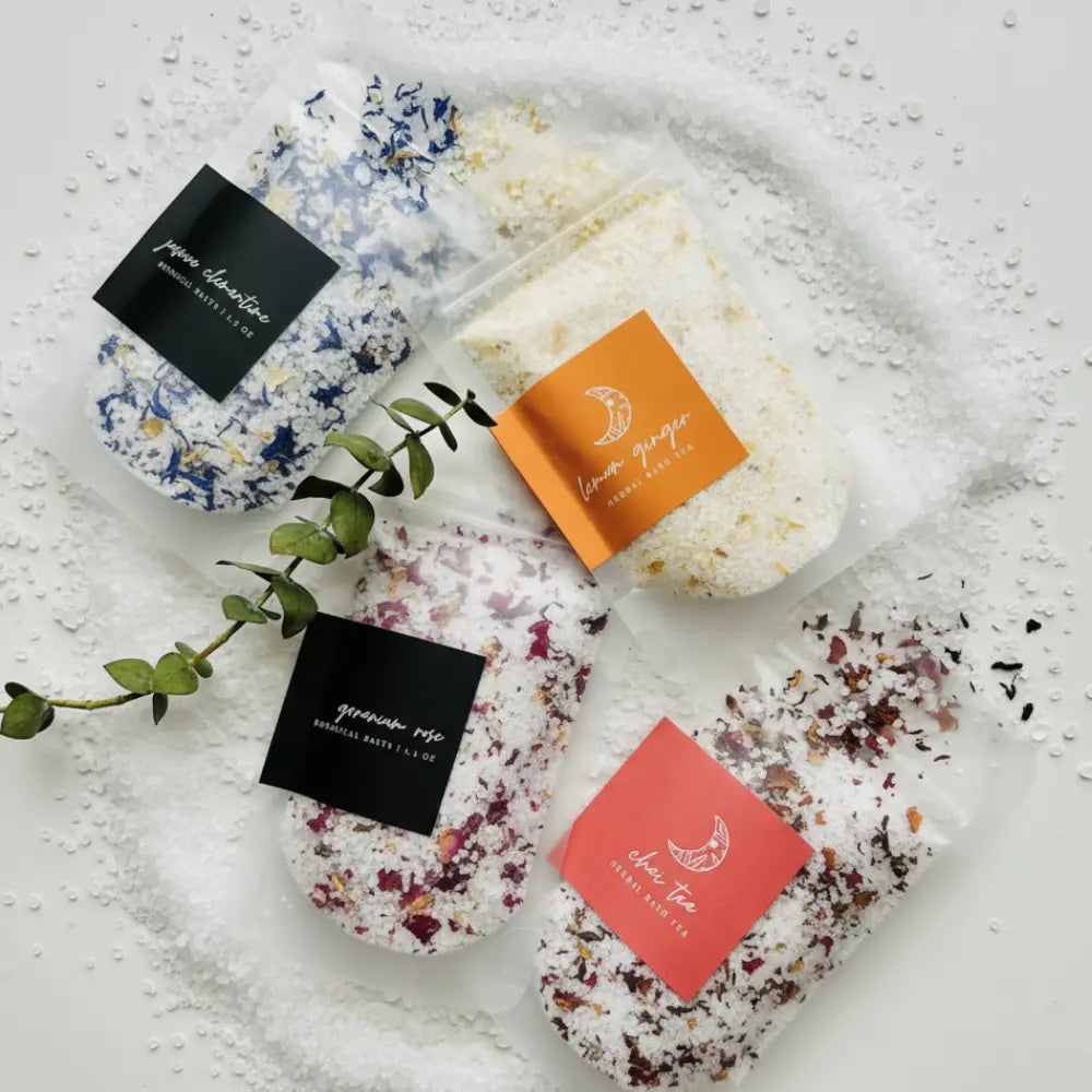Four bath salts with decorative packaging on a textured surface