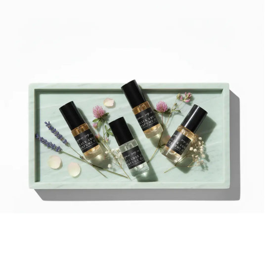 Four small bottles with black labels on a light green tray with flowers and leaves.