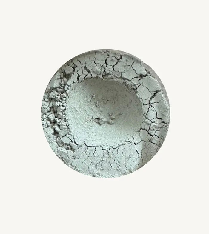 A photo of Pure Anada's Velvet Matte Loose Eyeshadow in Chambray which is a light silvery-gray with a hint of green on a tan background.