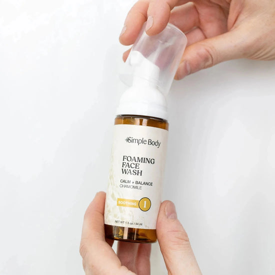 Hands holding a Simple Body Chamomile Face Wash travel size on a white background.