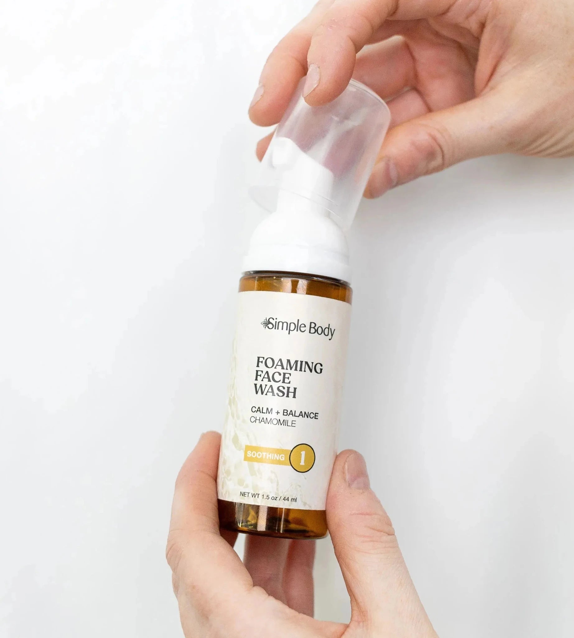 Hands holding a Simple Body Chamomile Face Wash travel size on a white background.