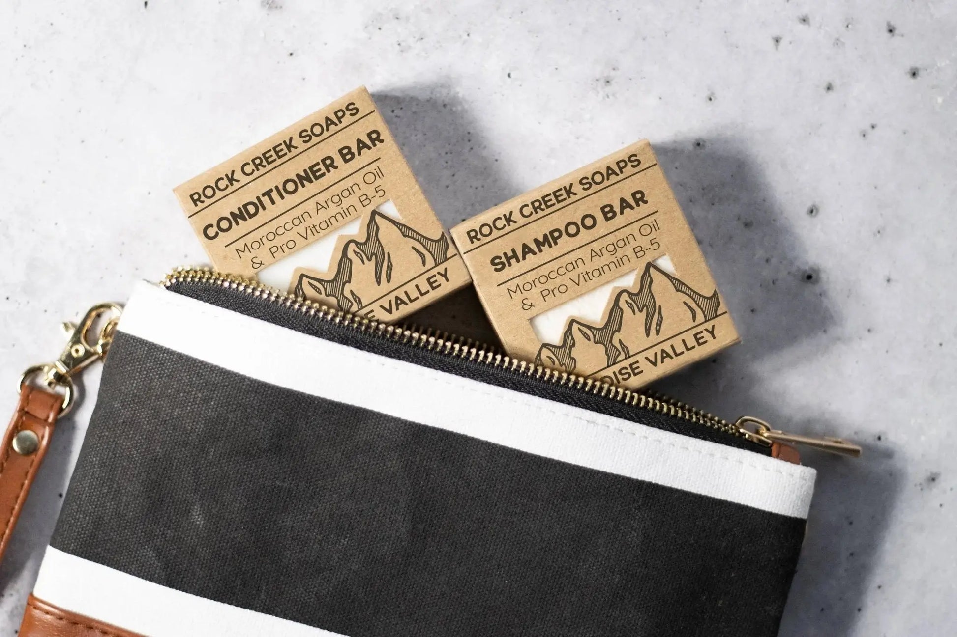 Two soap bars from Rock Creek Soaps on a gray surface with a black pouch.