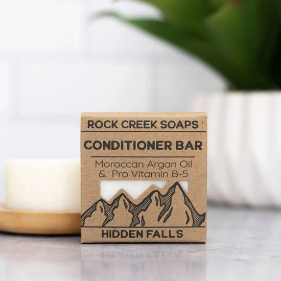Rock Creek Soaps conditioner bar packaging with a candle and plant in the background