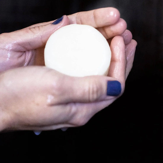 Hand holding a white bar of soap against a black background