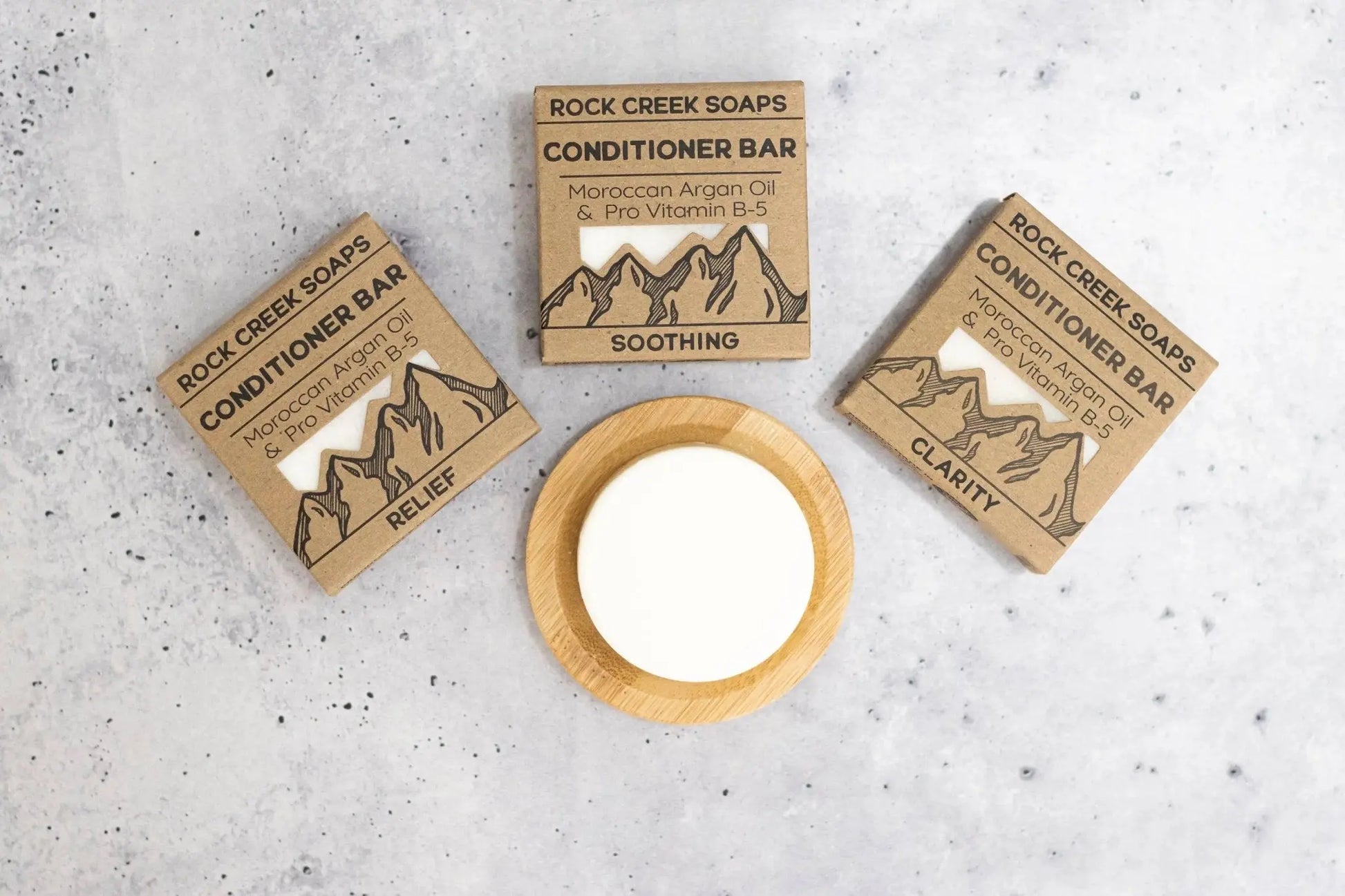 Three Rock Creek Soaps conditioner bars with packaging on a gray surface