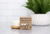Rock Creek Soaps conditioner bar packaging on a surface with a candle and plant in the background