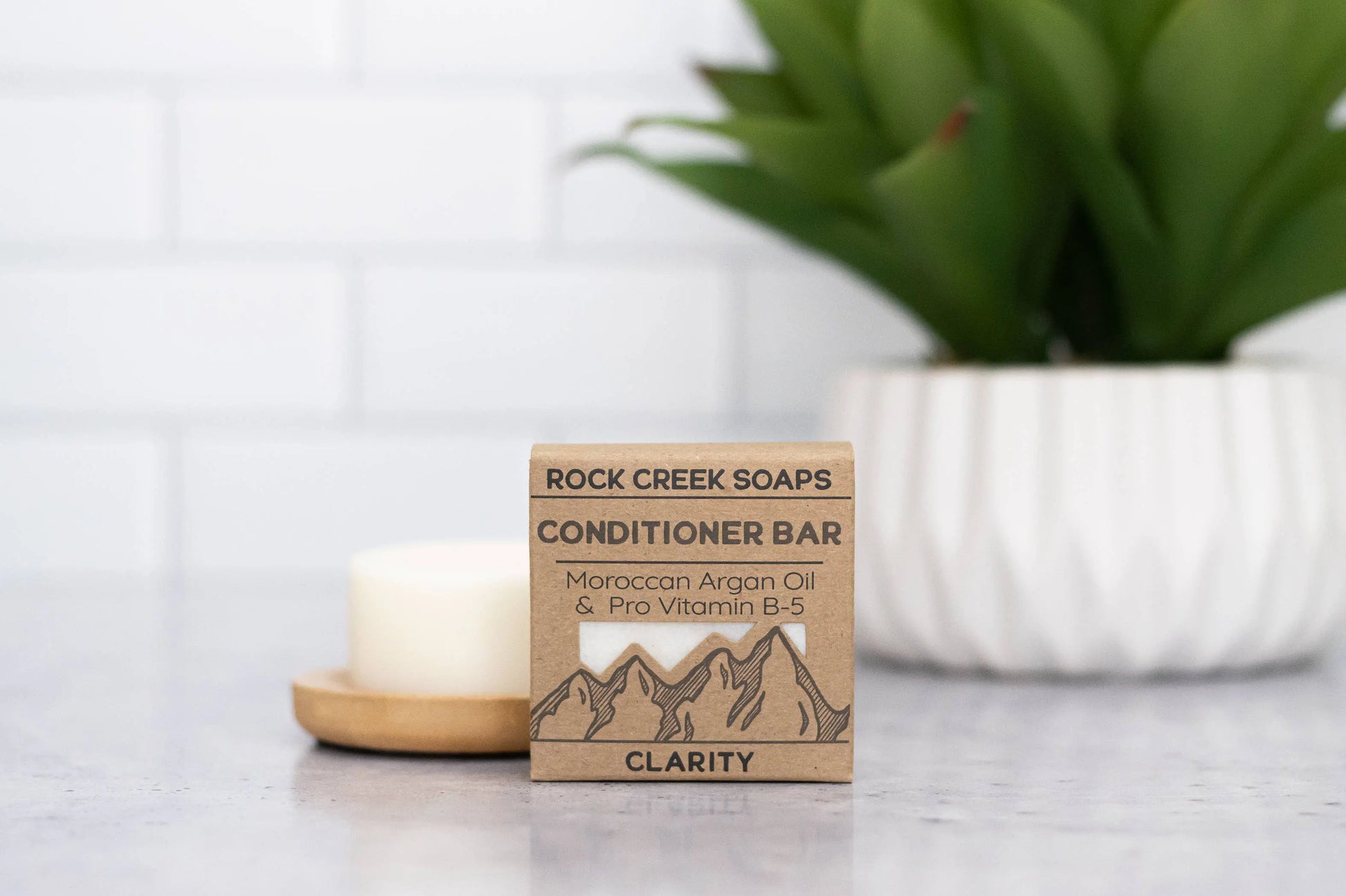 Rock Creek Soaps conditioner bar packaging on a surface with a candle and plant in the background