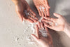 Four hands holding small amounts of white bath soak on a light surface