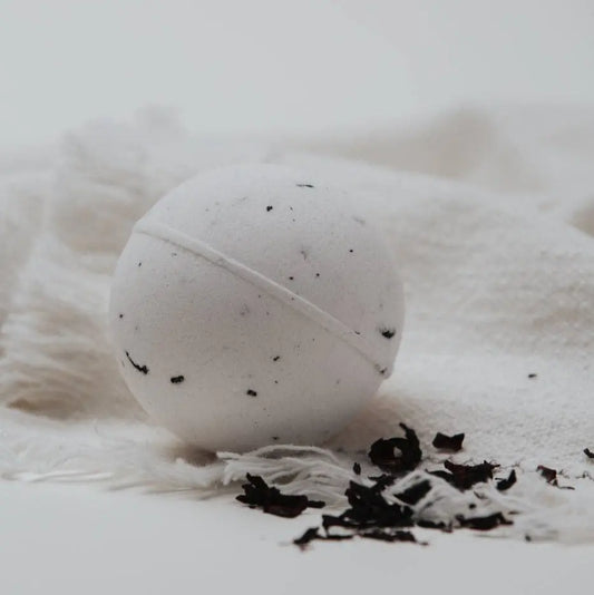 White bath bomb with hibiscus specks on a white fluffy surface