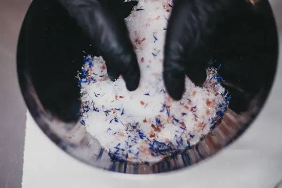 Close-up of hands wearing black gloves mixing colorful powder in a bowl.