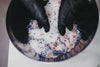 Close-up of hands wearing black gloves mixing colorful powder in a bowl.