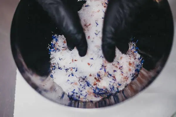 Close-up of hands wearing black gloves mixing colorful powder in a bowl.