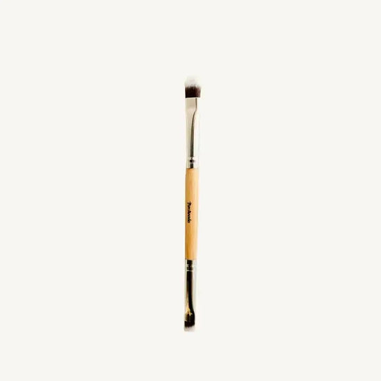A photo of Pure Anadas vegan Duo Makeup Brush with one side that is a soft, feathery brush and the other an angled brush with a wooden, natural handle on a tan background.