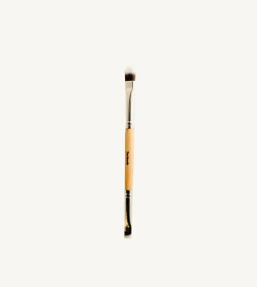 A photo of Pure Anadas vegan Duo Makeup Brush with one side that is a soft, feathery brush and the other an angled brush with a wooden, natural handle on a tan background.