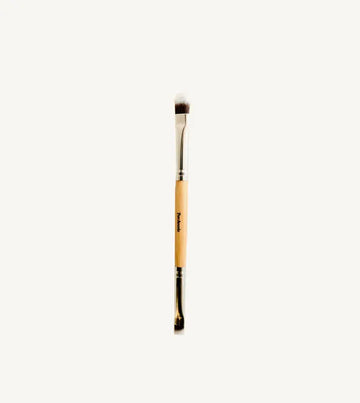 A photo of Pure Anadas vegan Duo Makeup Brush with one side that is a soft, feathery brush and the other an angled brush with a wooden, natural handle on a tan background.