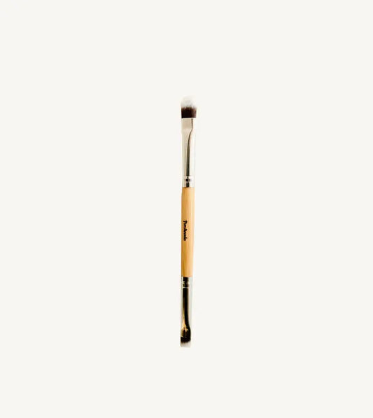 A photo of Pure Anadas vegan Duo Makeup Brush with one side that is a soft, feathery brush and the other an angled brush with a wooden, natural handle on a tan background.