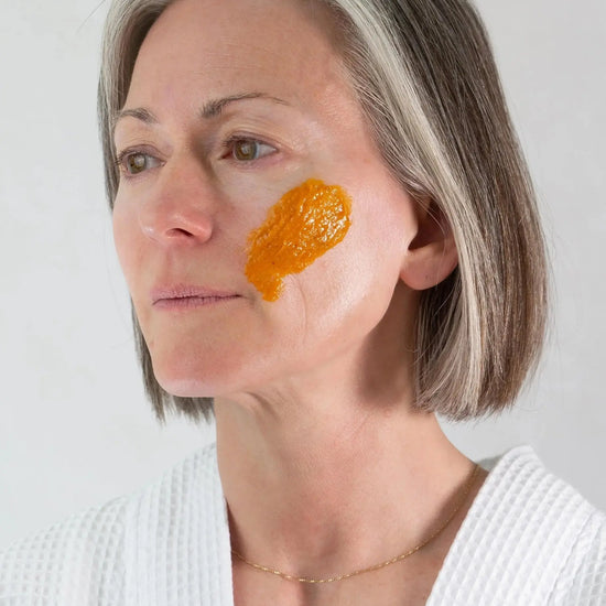 Woman with an swipe of Simple Body Pumpkin Enzyme Mask applied to her cheek against a plain background.