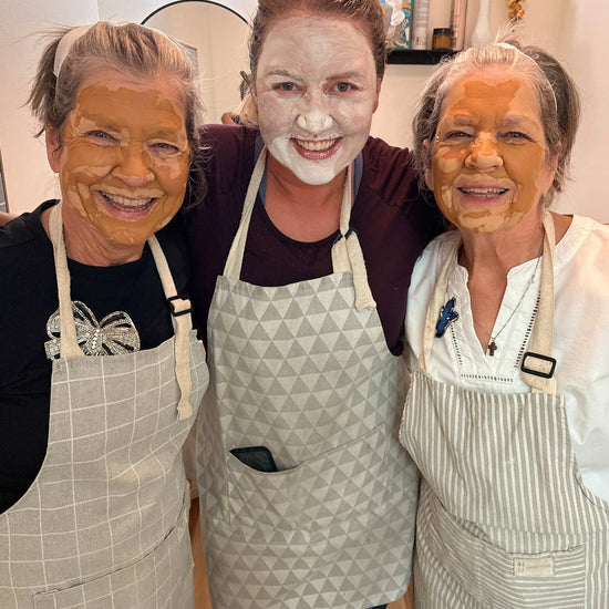 Three people with Simple Body Clay face masks on, wearing aprons, in a bathrom setting.