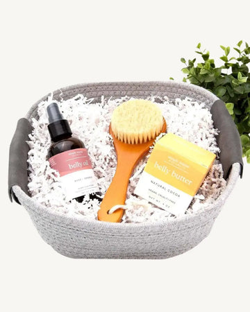 A gift basket containing a hydrating belly oil, a belly butter, and a dry brush, packaged in a reusable cotton rope basket.