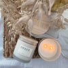 Candle with 'AMBER' label and 'Riley + Wheat' jar on a textured surface