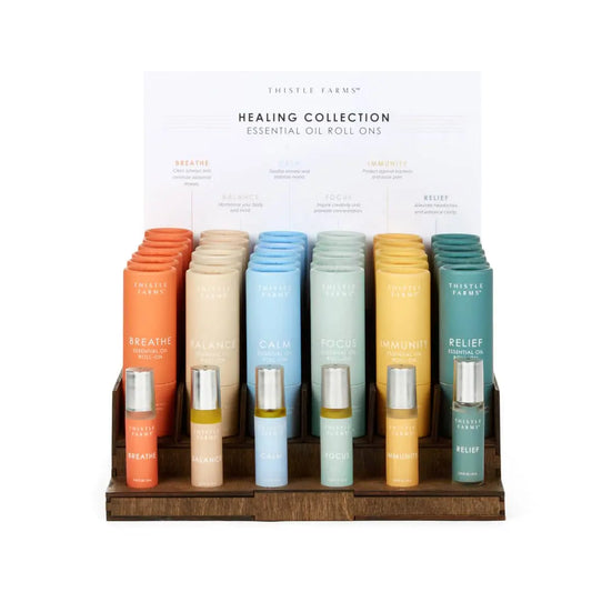 Thistle Farms Healing Collection essential oil roll-ons displayed on a wooden stand.