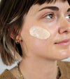 Woman with a patch of Simple Body Face Cream on her face against a neutral background