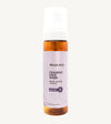 An amber colored pump bottle of Simple Body Foaming Face Wash with a purple label that says "Relax + Soothe+